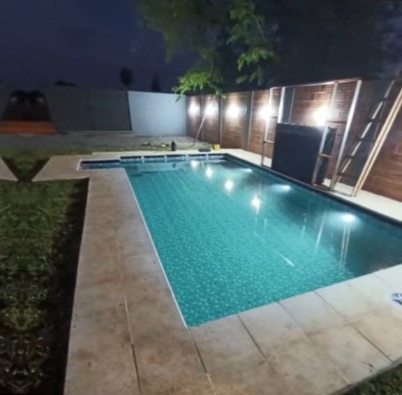 Piscina iluminada de noche junto al jardín